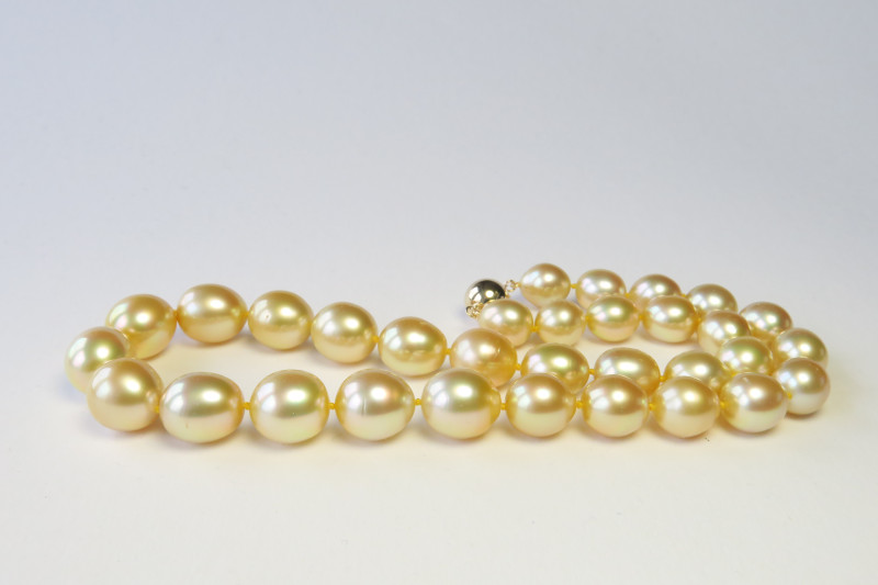 Eine edle leicht tropfenfoermige goldene Suedseeperlenkette mit warmem Farbton die minimale punktuelle Wachstumsmerkmale aufweist.