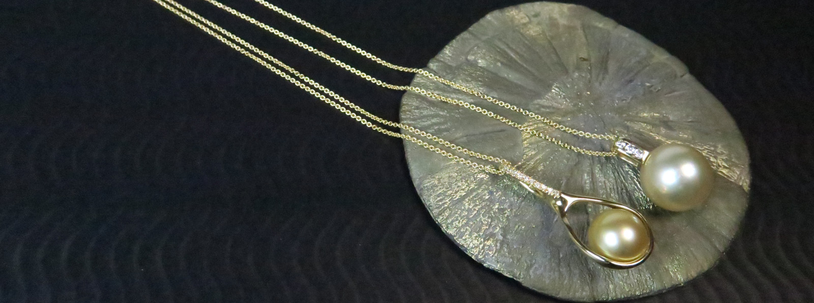 Die Südsee-Kollektion – Kostbarkeiten in Weiß und Gold Luxuriöse goldene Südseeperlen als Halsketten an feinen Goldketten, präsentiert auf einer glänzenden Pyrit-Mineralienscheibe.