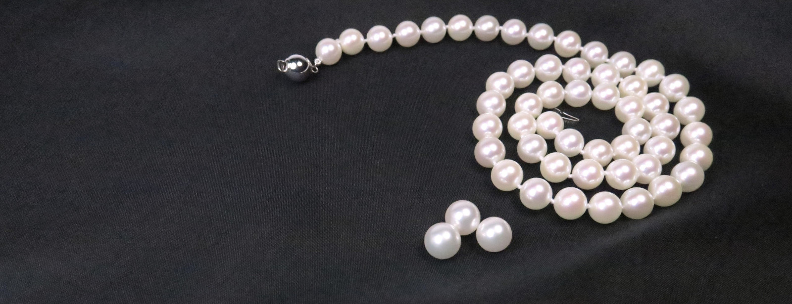 Das Erbe Japans – Exklusive Akoyaperlen Klassische japanische Akoyaperlen als weiße Perlenkette mit makellosem, tiefem Glanz auf elegant drapiertem, dunklem Stoff.