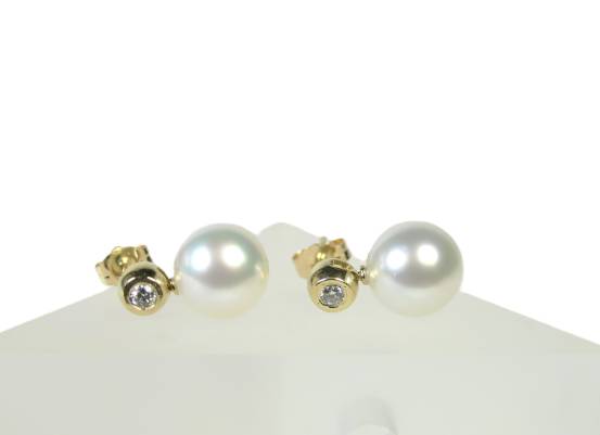 Das edle Paar Südsee-Perlenohrringe flach liegend auf heller Unterlage, die diamantbesetzten 14k Gelbgold-Stecker zeigen nach rechts.