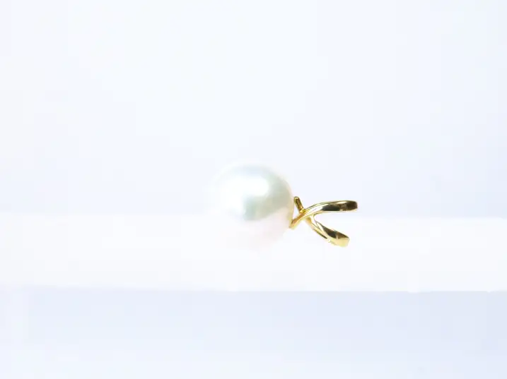 Der edle, geschwungene Perlenanhänger aus 585 Gelbgold flach auf einem Glasblock fotografiert, die filigrane Gold-Öse zeigt nach rechts.
