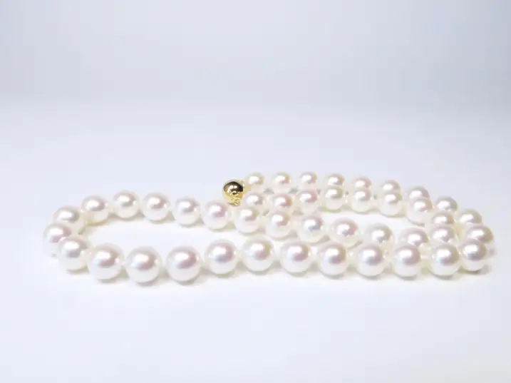 Japanische Akoya-Perlenkette im Durchmesser 9 bis 9,5 mm in AAA-Qualität, liegend auf weißem Untergrund mit der 14k Gelbgoldschließe hinten links