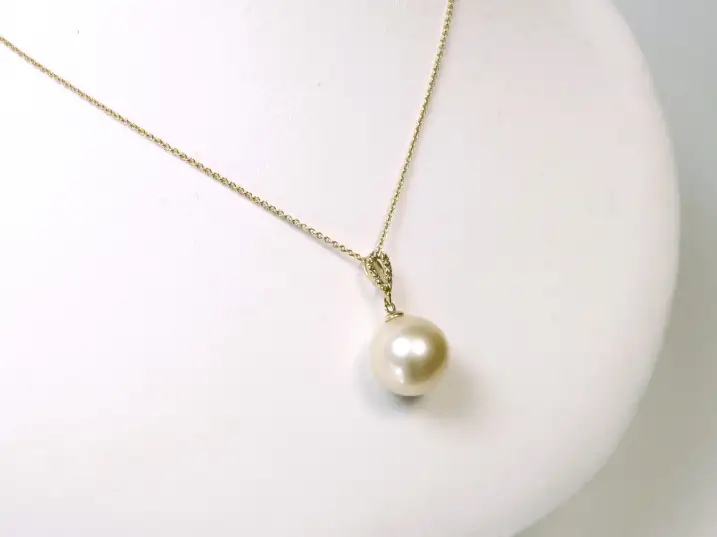Exklusiver Südsee-Perlenanhänger mit Diamanten in Gelbgold auf einer Präsentationsbüste von halb links fotografiert.