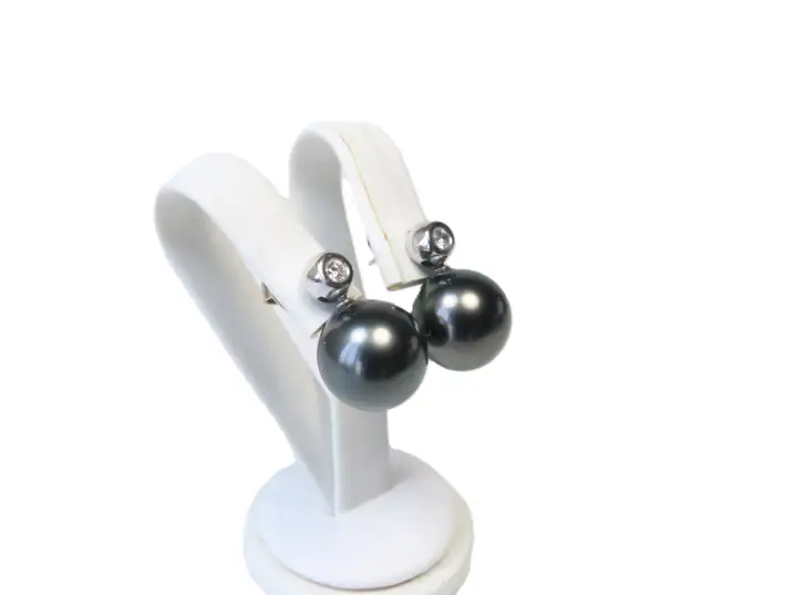 Exklusiver Perlohrschmuck mit runden Tahiti-Kulturperlen und feinen Diamantsteckern, Perspektive von halblinks auf einem Ohrständer.